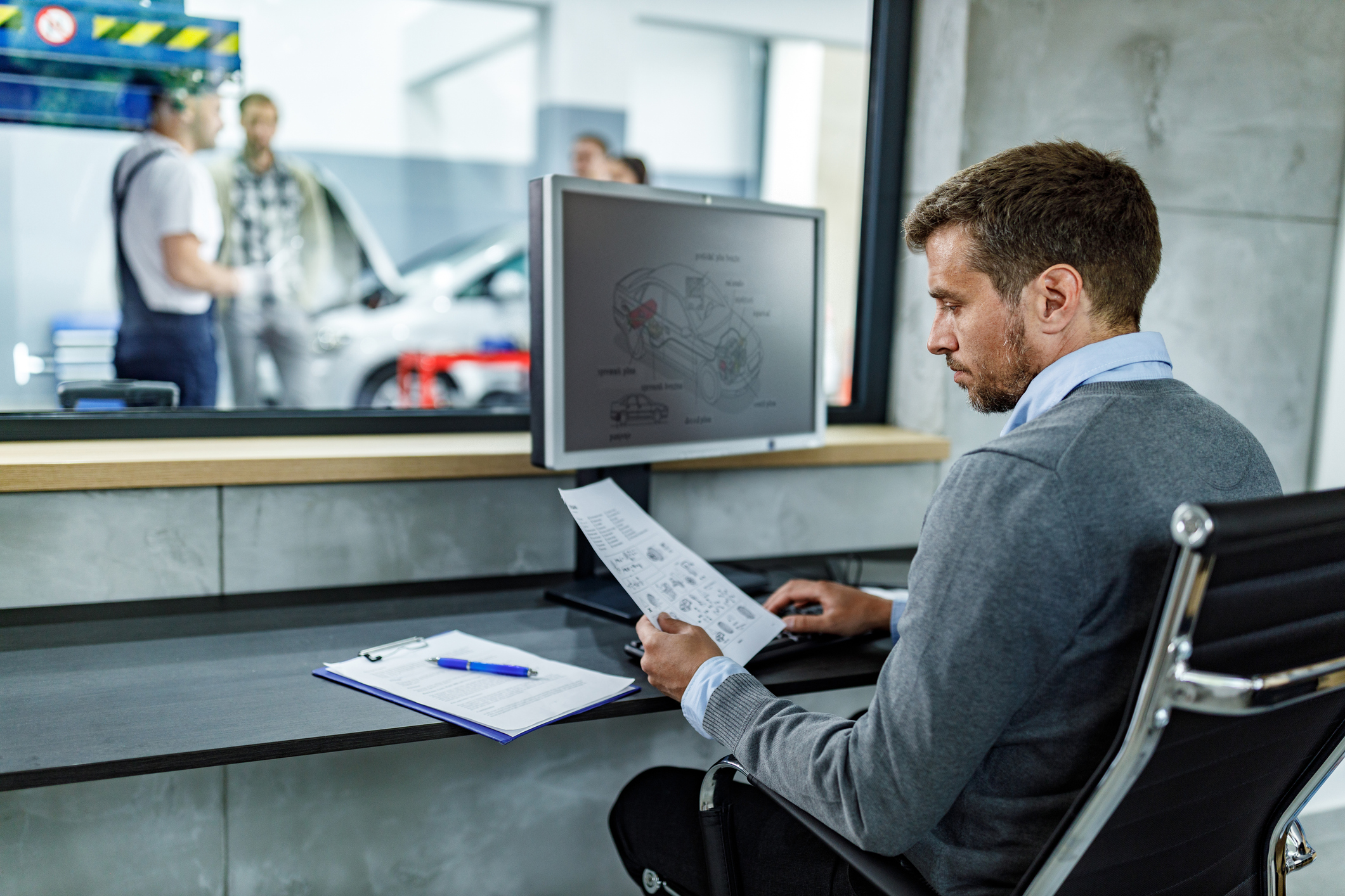 Mid adult foreman working on plans and PC in auto repair office.